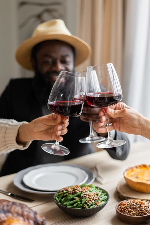 Free Crop content adult multiracial friends clinking glasses of wine while having festive dinner together at wooden table with tasty meals Stock Photo
