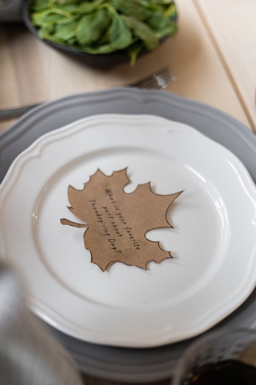 Free From above of cardboard postcard cutout in shape of maple leaf with inscription on Thanksgiving Day placed on porcelain plate on table for dinner Stock Photo