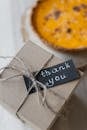 High angle of cardboard present box tied with rope and decorated with small postcard with Thank You inscription place on table near pie on Thanksgiving