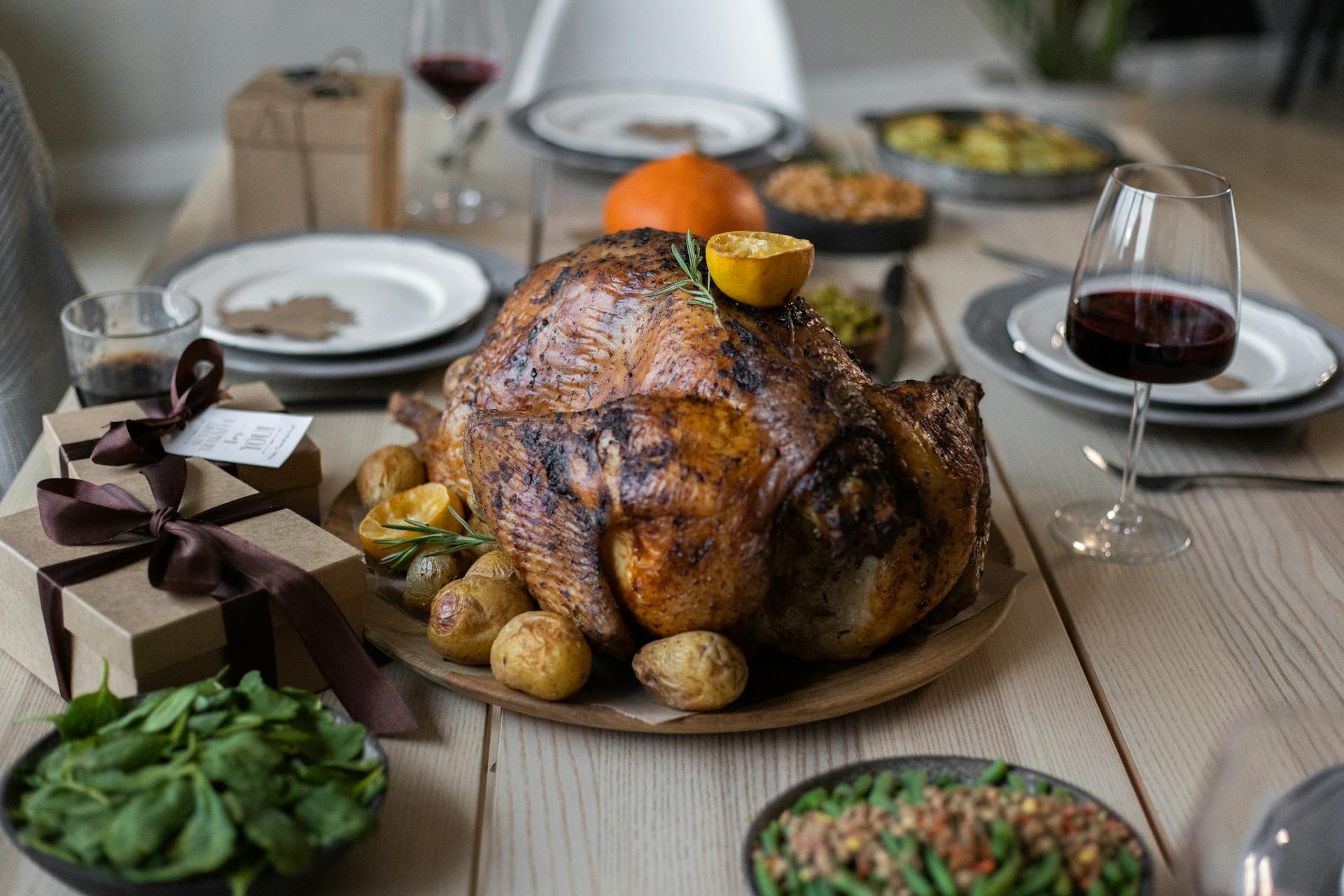 High angle of appetizing roasted turkey and glasses of wine with other dishes placed on wooden table prepared for celebrating Thanksgiving Day