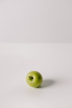 A single green apple placed on a white surface with ample copy space, highlighting minimalist simplicity.
