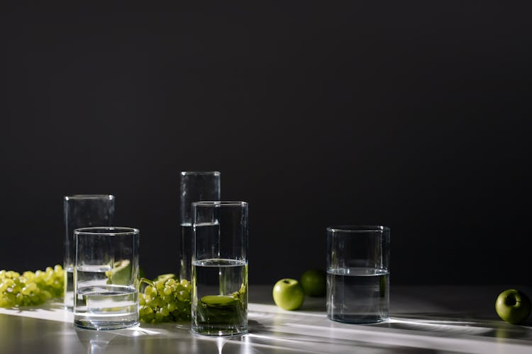 Glasses Of Water And Green Fruits On A White Surface