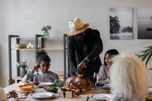 Free Happy multiracial adult friends sitting at table served with roasted turkey and other food while having Thanksgiving dinner Stock Photo