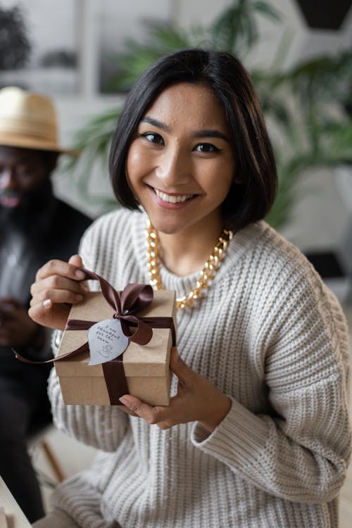 Женщина в белом вязаном свитере с коричневой подарочной коробкой
