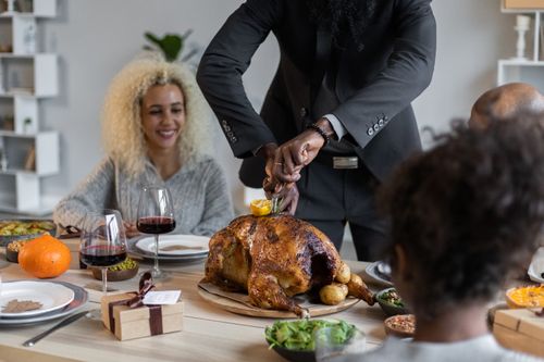Free Crop anonymous African American male cutting roasted turkey with knife and fork while having Thanksgiving dinner with diverse guests Stock Photo