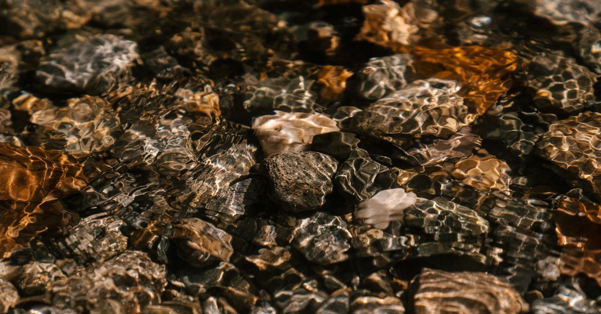 Crystal clear water at the base of a waterfall with rocks visible underwater