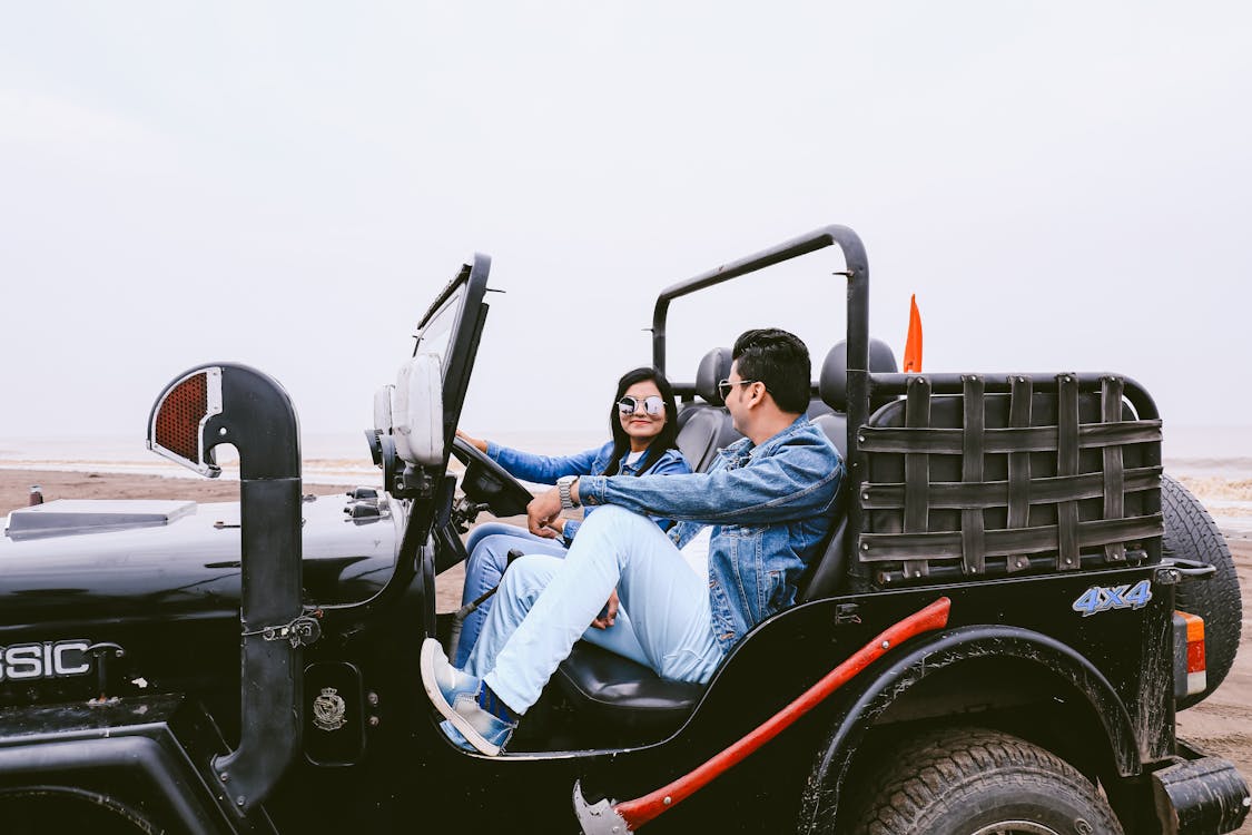 Free Side view of couple in denim clothes looking at each other sitting in off road car Stock Photo