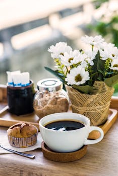 A charming breakfast table with black coffee, muffin, sugar jar and floral decor in natural light.