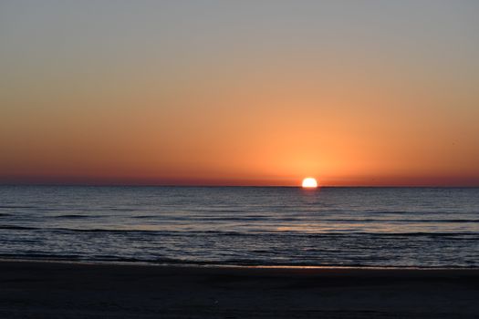 A tranquil sunset over the ocean captured at the beach, perfect for a serene landscape wallpaper.