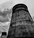 Low angle black and white of aged weathered evaporative cooling towers located in industrial area against cloudy sky