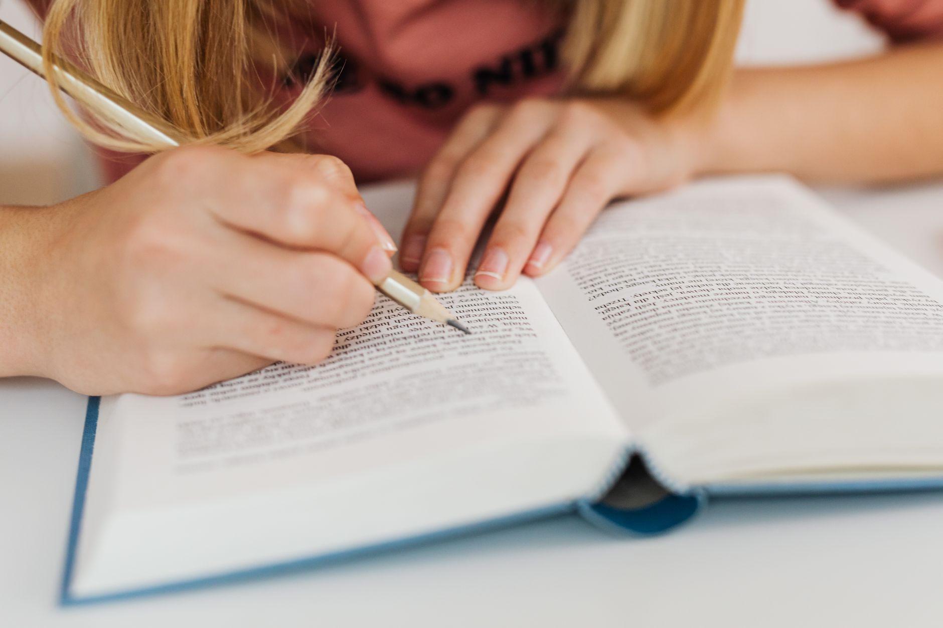 Close-up of a woman's hands writing notes in an open book indoors.