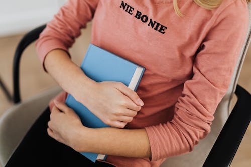 Woman in Pink Long Sleeve Shirt Holding Blue Book