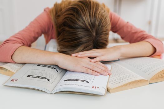 一名因学业压力而不知所措的学生，在课桌上摊开的书本前睡着了，这体现了学习的疲惫