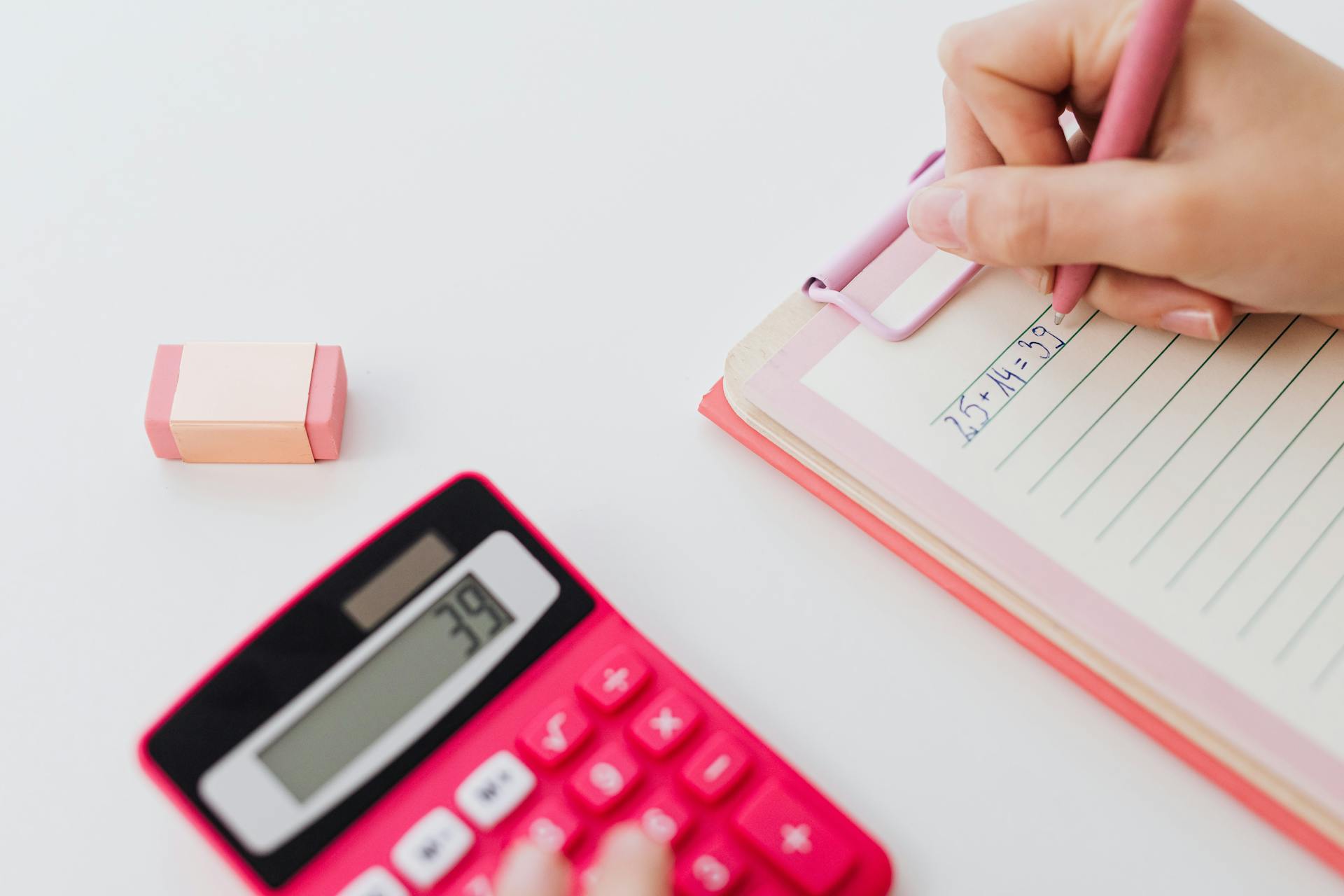 Close-up of hands using a calculator and writing equations on a notebook, perfect for math concepts.