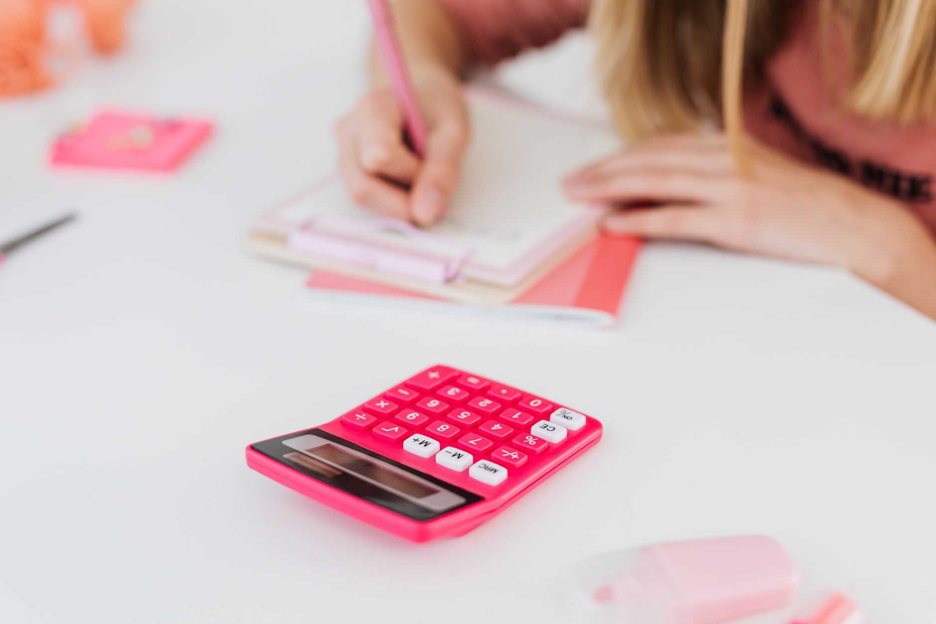 A young student writing in a notebook with a pink calculator nearby, focusing on homework.