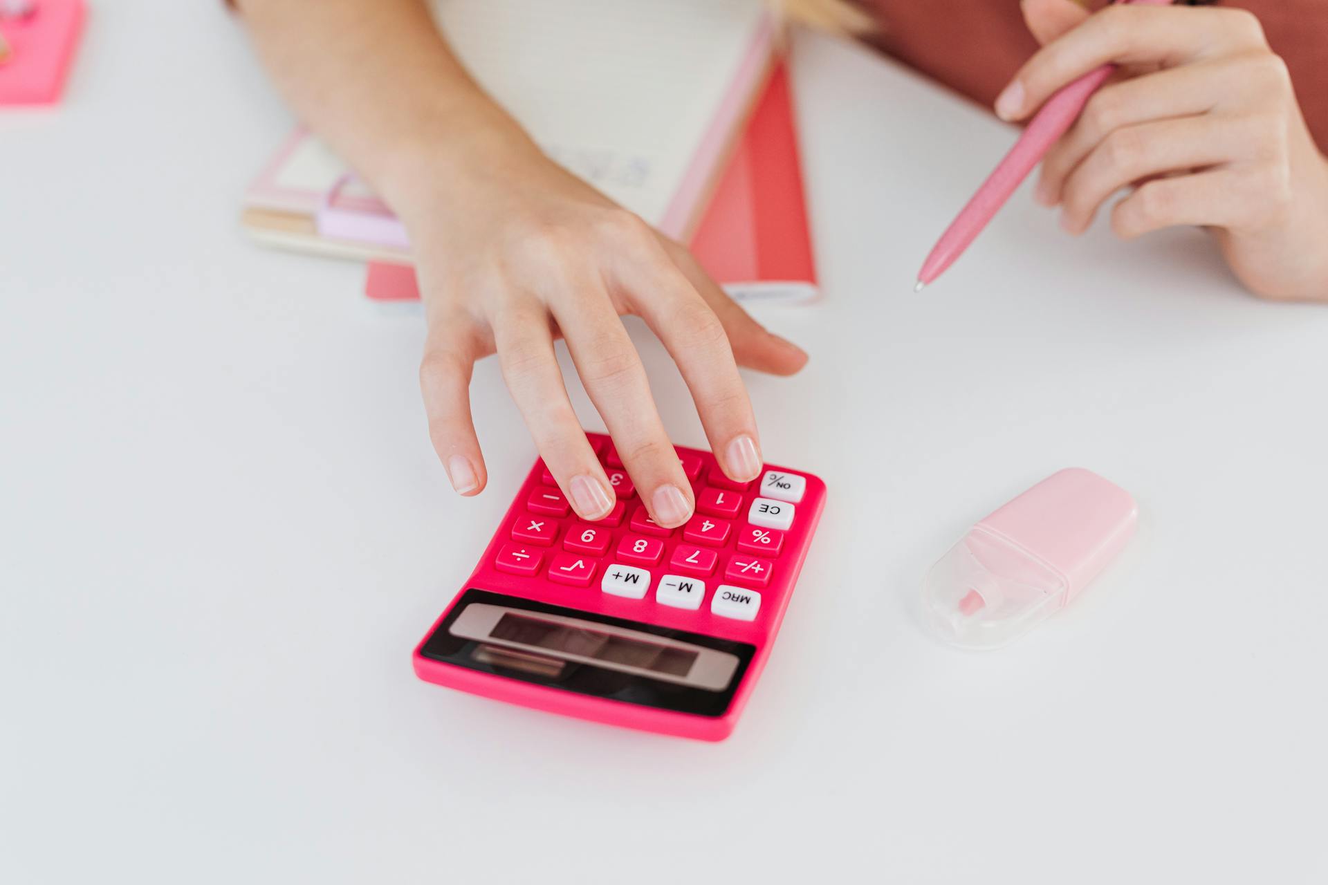 Close-up of hands using a pink calculator with notebooks and erasers, perfect for education and finance themes.