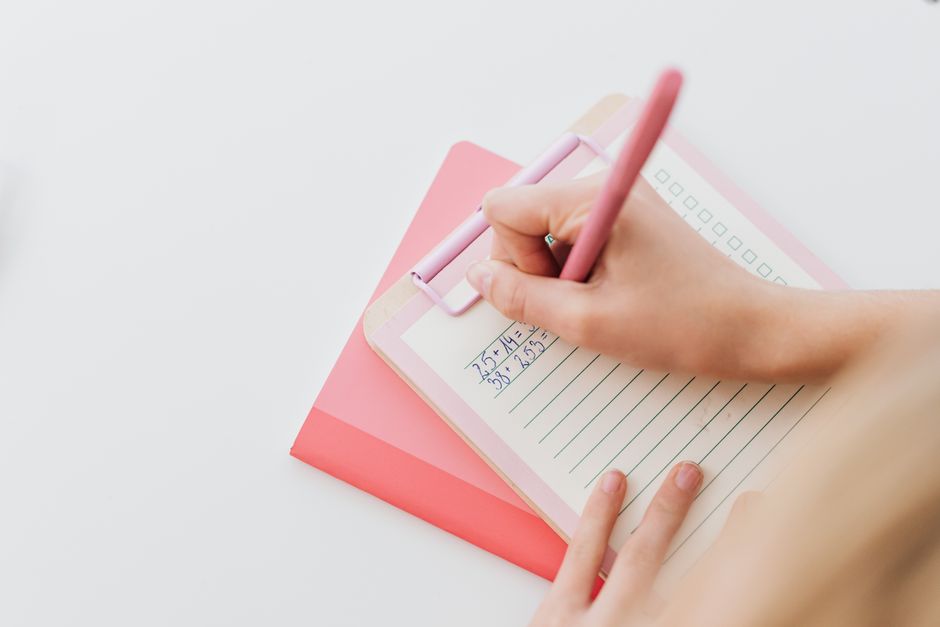 Close-up of person solving math equations on a pink clipboard with a pen.