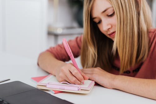 Free A focused young woman writing in a notebook indoors, showcasing creativity and study habits. Stock Photo