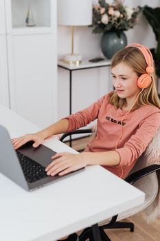 A teenage girl wearing headphones and using a laptop at home. Cozy indoor setup with casual attire.