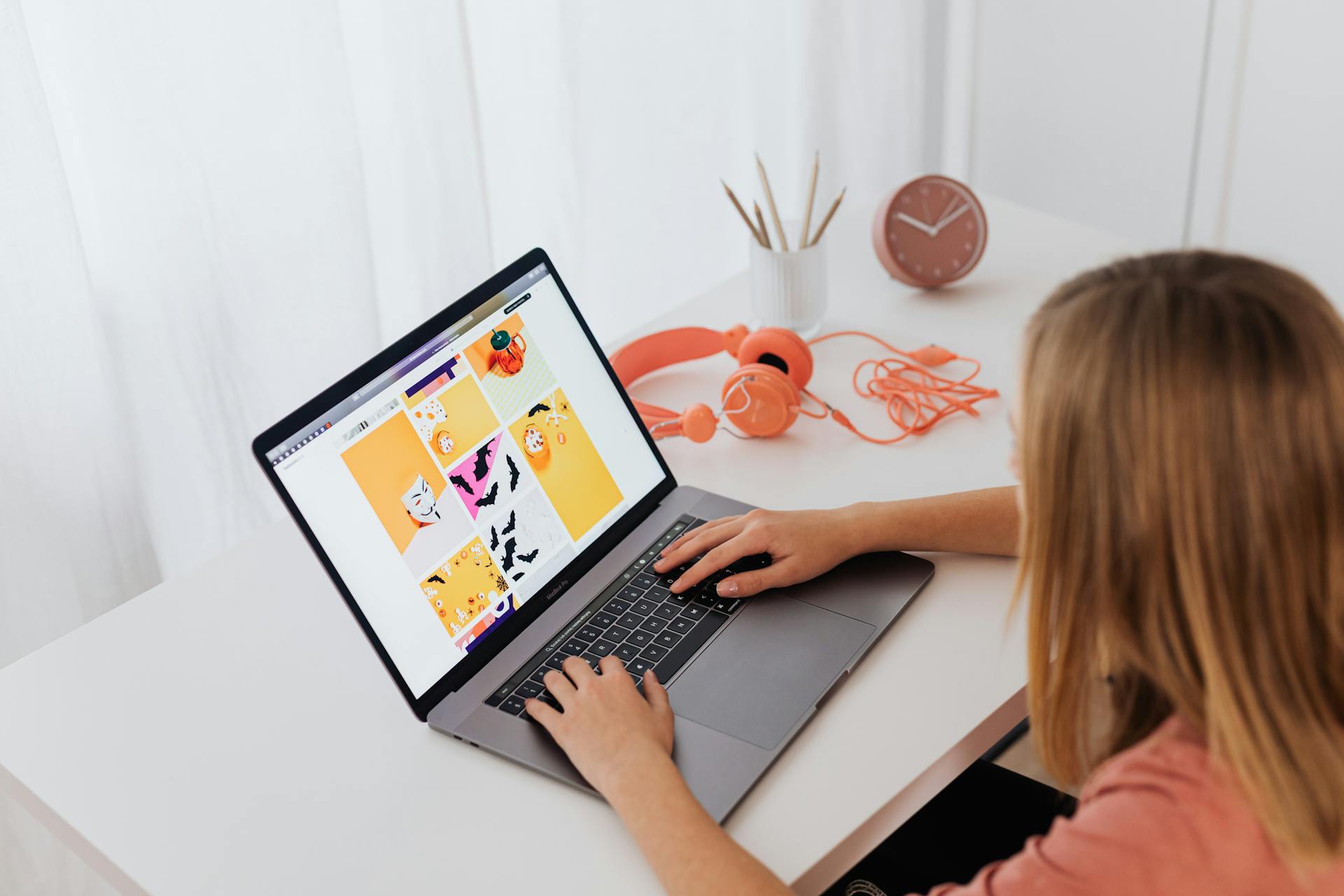 Woman creating digital art using a laptop at a stylish desk with headphones and clock.