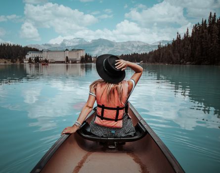 A woman in a black hat and life vest paddles a canoe on picturesque Lake Louise in Canada.