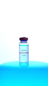 A close-up of a vaccine vial labeled 'Virus' against a blue backdrop.