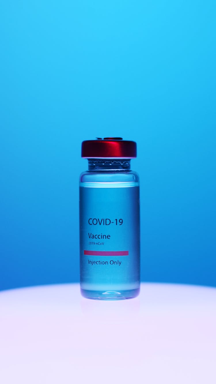 A Close-Up View Of A Covid-19 Vaccine Vial On Blue Background