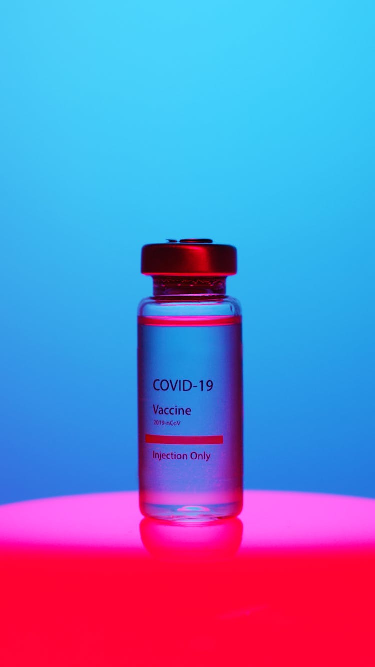 A Close-Up View Of A Covid-19 Vaccine Vial On Blue Background