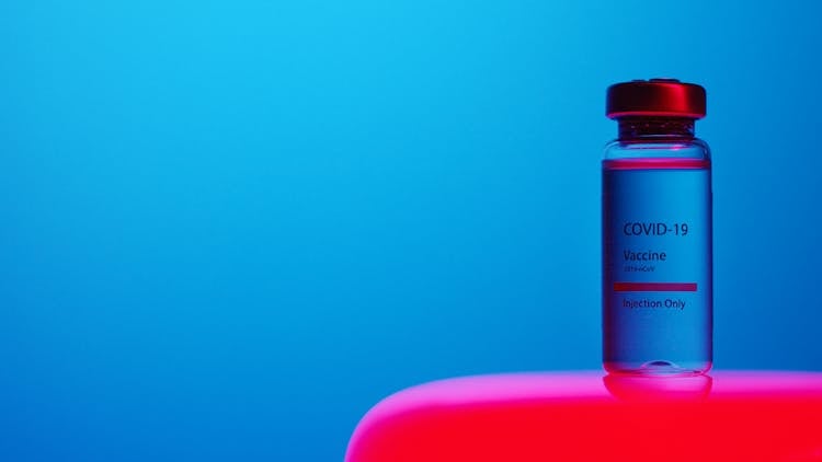 A Close-Up View Of A Covid-19 Vaccine Vial On Blue Background