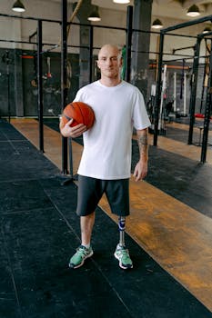 A bald man stands confidently in a gym holding a basketball, showcasing strength and empowerment.