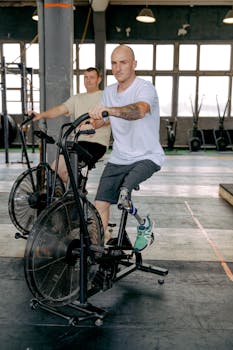 Two men working out on stationary bikes in a gym, one with a prosthetic leg.