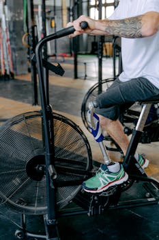 A tattooed man with a prosthetic leg working out on a stationary bike in a gym.