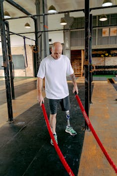 Man with prosthetic leg performing strength training with battle ropes in a gym.