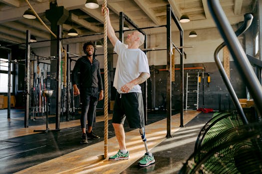 Two men engaged in adaptive fitness training with climbing ropes in a modern gym setting.