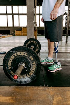 Man with a prosthetic leg stands ready to lift a barbell in an indoor gym setting.