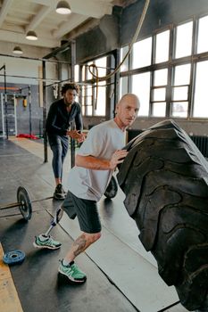 Two men exercising in gym with prosthetic leg and tire, showcasing determination and strength.