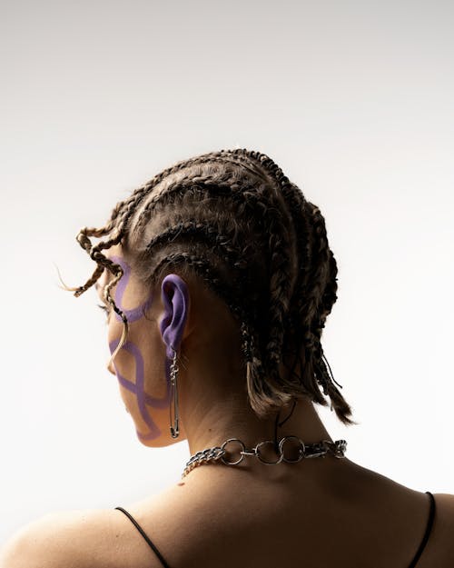 Back view young slim female with African braids hairstyle standing against white wall in studio and looking away