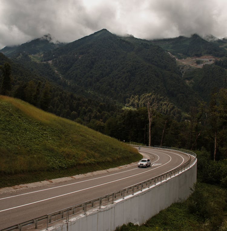 Car On Road Near High Green Mountains In Overcast Weather