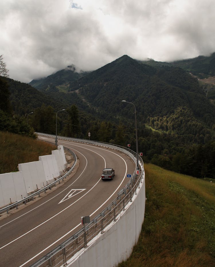 Auto Driving On Roadway Near Green Ridges Under Cloudy Sky