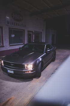 A sleek black Mustang parked under an industrial setting at night, showcasing luxury and design.