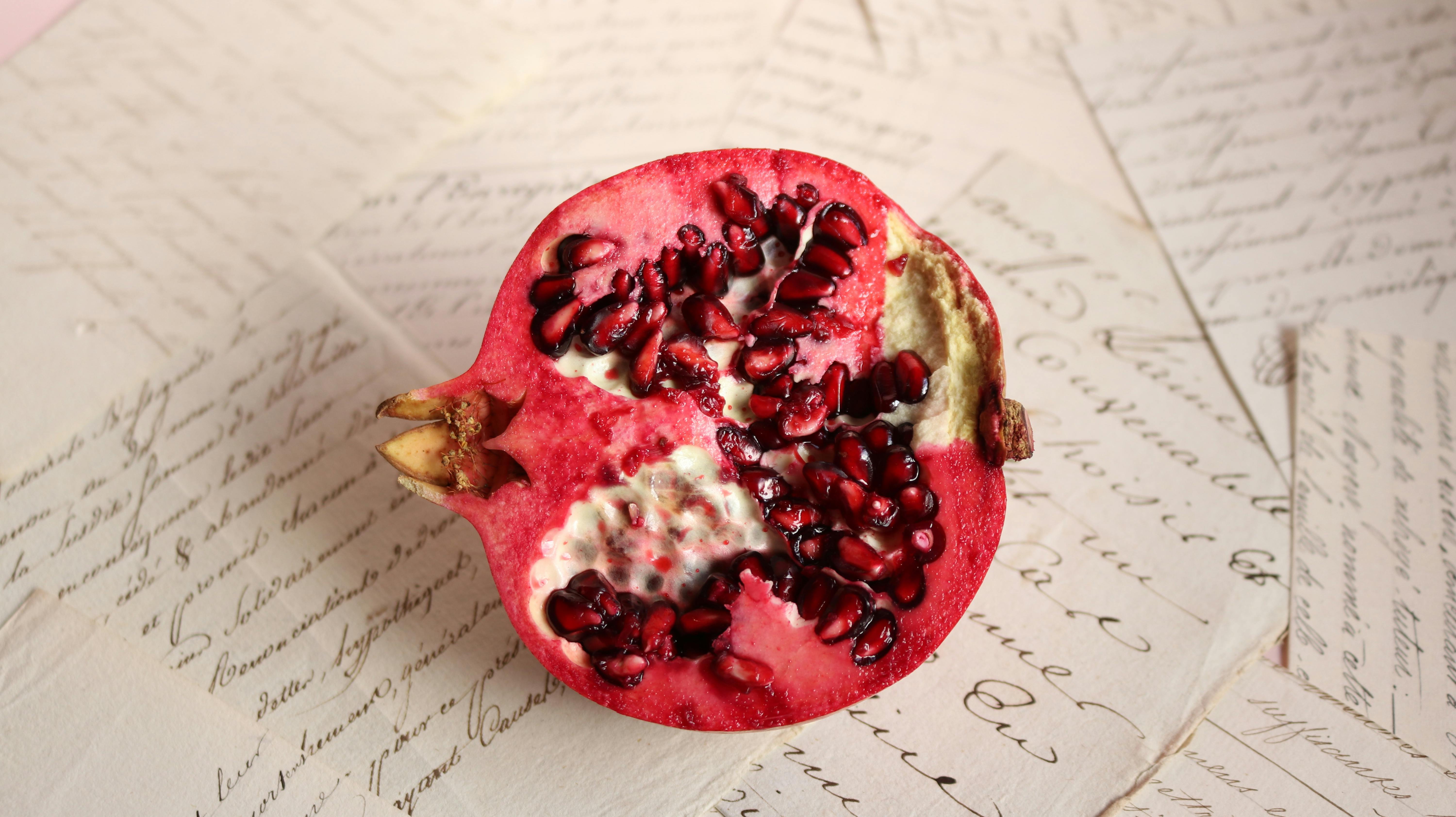 High angle shot of a sliced pomegranate on vintage papers showcasing vibrant seeds.