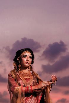 Portrait of a woman in traditional clothing with intricate jewelry, set against a vibrant sunset sky.
