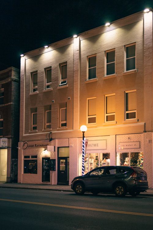 Free Contemporary automobile parked on asphalt roadway against house with shiny lights and inscriptions in night city Stock Photo