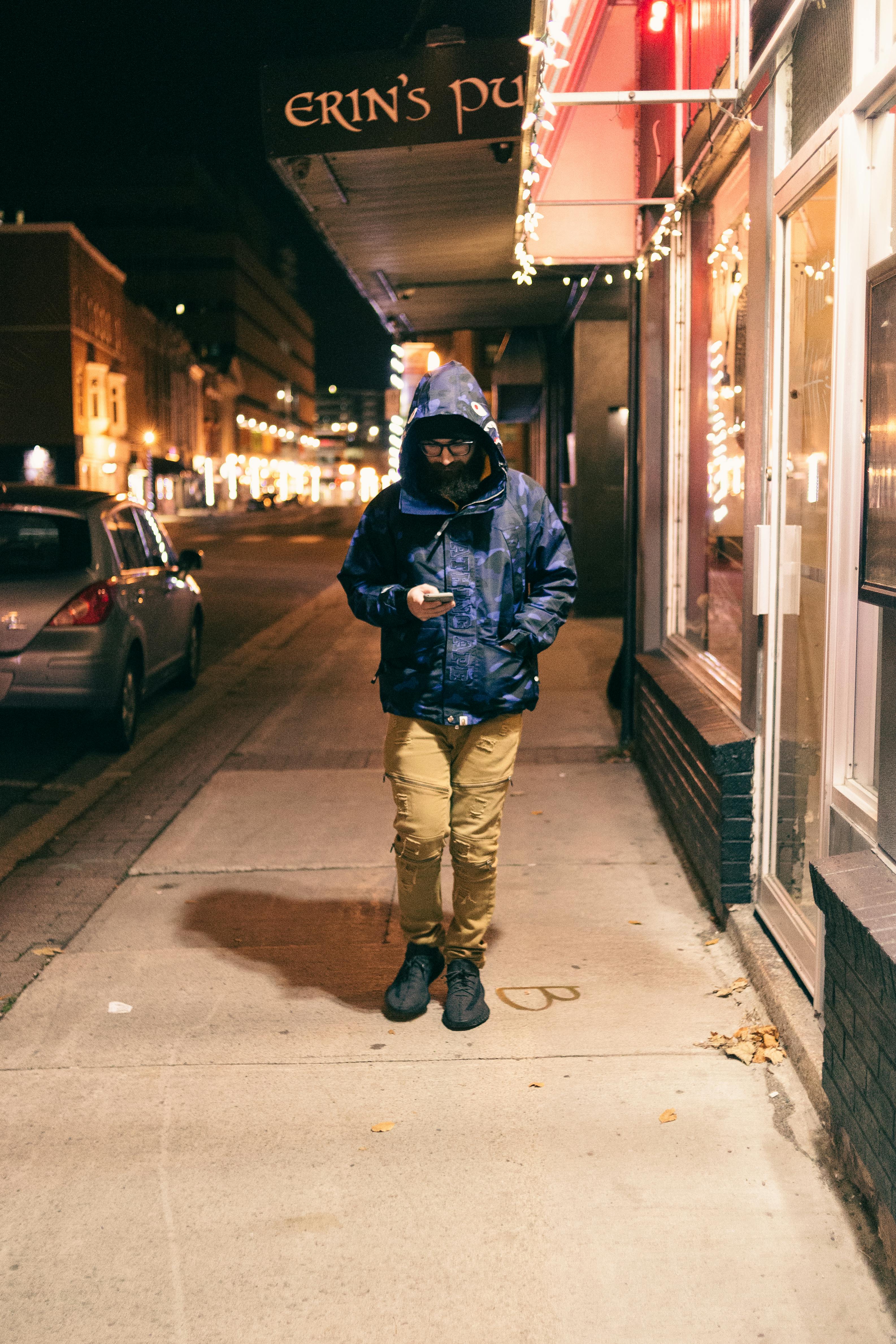 hipster man chatting on smartphone on pavement in night town