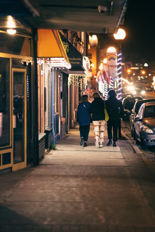 Free Back view of anonymous partners in outerwear strolling on walkway between buildings and roadway with shiny lights in evening city Stock Photo