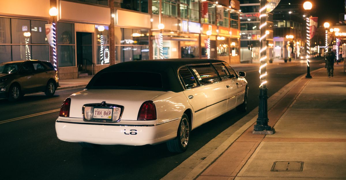 White limo with tinted glasses and license plate on roadway against buildings illuminated by street lights in evening city