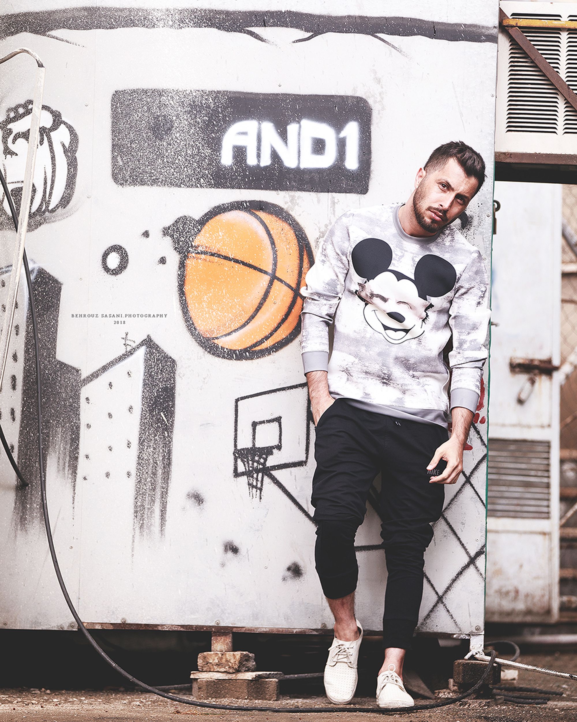 Casually dressed man poses with urban graffiti in Tehran for a stylish streetwear look.
