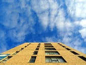 从低角度仰望现代摩天大楼，可见充满活力的蓝天与零散的云层