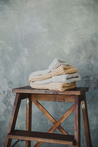 Folded hand-knitted socks stacked on a wooden stool — Ksenia Chernaya on Pexels