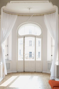 Bright and classic indoor view featuring elegant white French doors adorned with sheer white curtains.